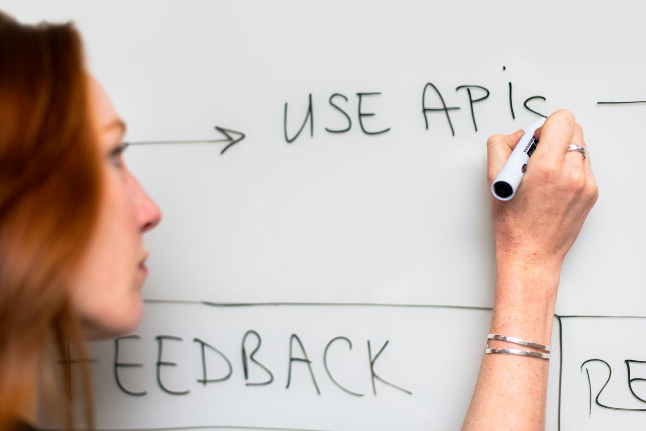 hero-img-01 A woman writes Use APIs on a whiteboard, focusing on software planning and strategy.